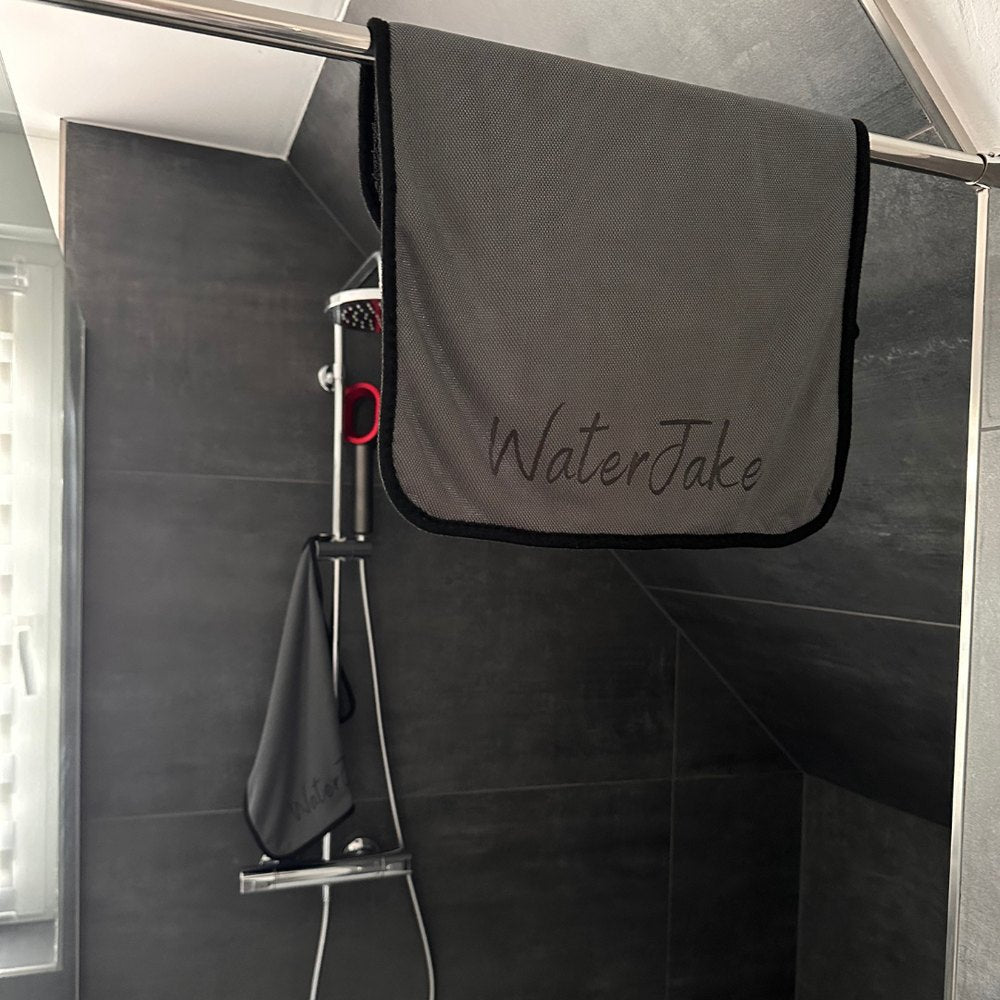 Graues WaterJake® Trockentuch hängt über der Duschwand, ein zweites an der Duscharmatur