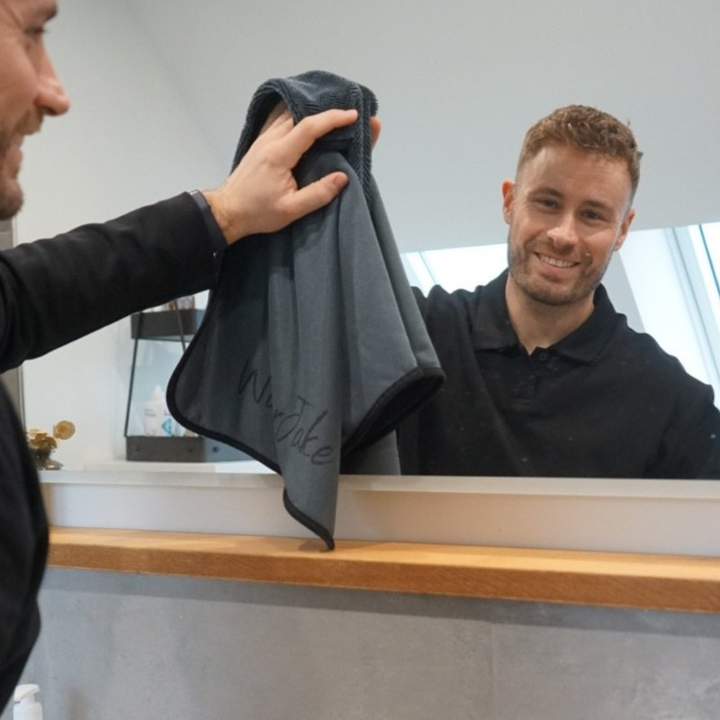 Junger Mann trocknet den Badspiegel mit dem WaterJake® Trockentuch